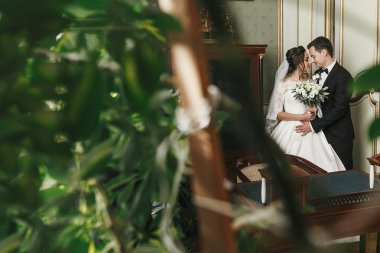 muhteşem gelin buketi ve şık damat yavaşça lüks otel odasında yeşil yaprakları arasında sarılma. zengin düğün çifti kucaklayan. Yeni evliler kapalı Klasik şehvetli anı