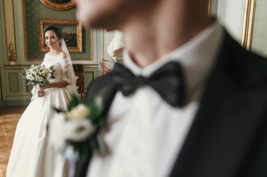 muhteşem gelin buketi ve şık damat lüks otel odasında poz ile şaşırtıcı elbiseli. zengin düğün çifti. Yeni evliler kapalı klasik romantik duygusal an