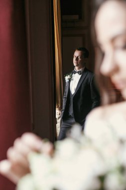 şık damat şaşırtıcı elbise içinde muhteşem gelin buket vasıl pencere lüks otel odasında poz ile bakarak. zengin düğün çifti. Yeni evliler kapalı klasik romantik anı