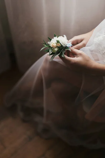 豪華な花嫁はローブの窓の近くに座っているブートニ エールを保持しています 美しい女性の結婚式の日の準備 花を持ってします 女の子の足とベール 官能的な瞬間 — ストック写真