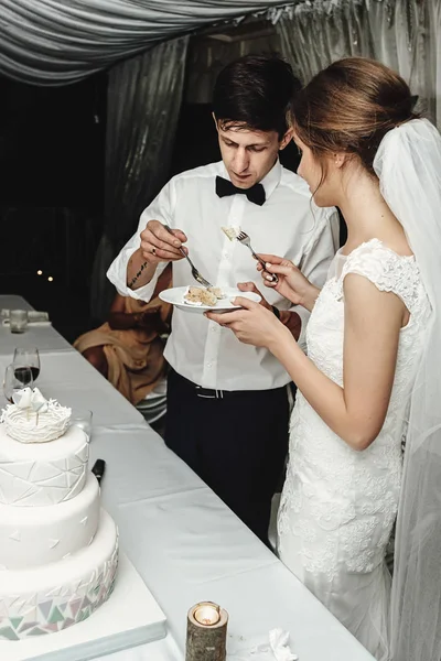 Stylish gorgeous bride and elegant groom cutting and tasting  unusual white wedding cake