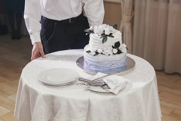 婚礼蛋糕服务员拿着带有白色和蓝色奶油和花卉装饰品的时尚婚礼蛋糕在餐厅举行的婚礼招待会上 — 图库照片