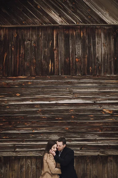 コートでスタイリッシュな新郎の木造の家で抱いてゴージャスな花嫁 優しくハグし 雪の降る公園での結婚式 納屋の結婚式 新婚夫婦のロマンチックな官能的な瞬間 — ストック写真