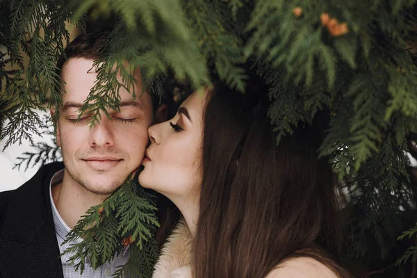 华丽的新婚情侣在冬季下雪的公园接吻 穿着大衣和新郎的时髦新娘在冬季森林里拥抱绿树 新婚夫妇浪漫的感性时刻 — 图库照片