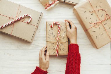 şık yılbaşı hediyesi şeker kamışı ve kırmızı kurdele ile tutan eller. düz yatıyordu. Beyaz ahşap zemin üzerinde modern craft hediyeler. mevsimlik selamlar. neşeli Noel kavramı