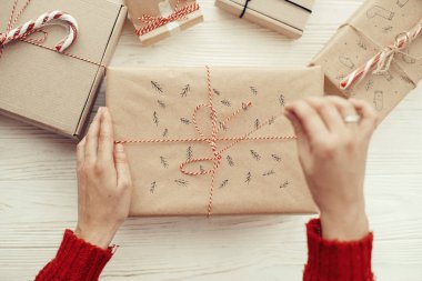 şık yılbaşı hediyesi kırmızı kurdele ile açılış eller. Beyaz ahşap zemin üzerinde modern craft hediyeler. neşeli Noel kavramı. mevsimlik selamlar