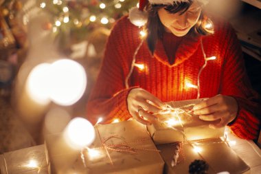 mutlu Noeller. Noel sarma kız ağaç aydınlatma altında Festival oda akşam ışıklar sunar. şeker kamışı ile modern craft hediye açılış santa şapkalı kız. atmosferik an