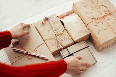 Şık Noel kaydırma eller kırmızı kurdele ile mevcut. Beyaz ahşap zemin üzerinde modern craft hediyeler. neşeli Noel kavramı.