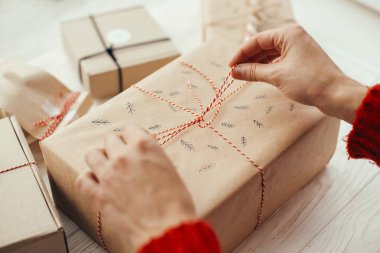 Şık Noel kaydırma eller kırmızı kurdele ile mevcut. Beyaz ahşap zemin üzerinde modern craft hediyeler. neşeli Noel kavramı.