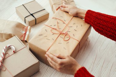 Şık Noel kaydırma eller kırmızı kurdele ile mevcut. Beyaz ahşap zemin üzerinde modern craft hediyeler. neşeli Noel kavramı.