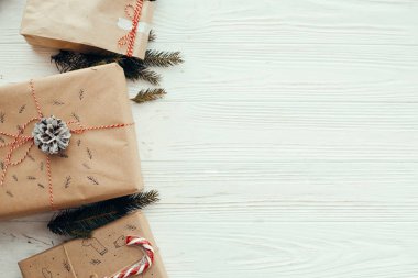 şık basit Noel kırmızı kurdele, şeker kamışı, Çamın dalları ve koniler ile sunar. Modern craft hediyeler düz beyaz ahşap zemin üzerinde yatıyordu. mevsimlik tebrik kartı.