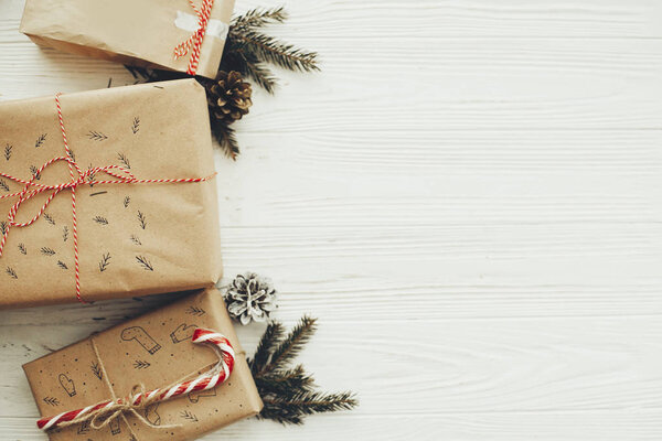 стильные простые рождественские подарки с красной лентой, леденцовой тростью, сосновыми ветвями, местом для текста. современные подарки ремесла на белом деревянном фоне, квартира лежала. поздравительная открытка
.
