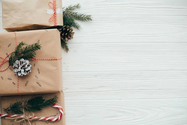 şık basit Noel hediyesi ile kırmızı kurdele, şeker kamışı, Çamın dalları, metin için yer. Modern craft hediyeler düz beyaz ahşap zemin üzerinde yatıyordu. mevsimlik tebrik kartı.