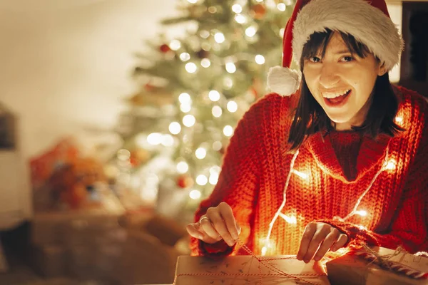 Happy Girl Santa Hat Red Sweater Wrapping Christmas Presents Lights — Stock Photo, Image