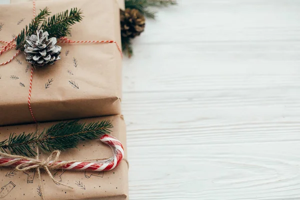 メリー クリスマスのコンセプトです スタイリッシュなプレゼントに赤いリボン キャンディーの杖 松の枝 コーン 白い木製の背景 テキストのためのスペースの現代クラフト ギフト 季節の挨拶 — ストック写真