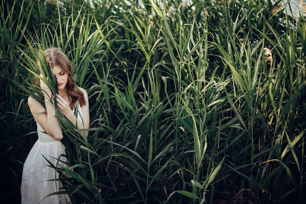 Beautiful boho girl embracing grass posing in white dress in green cane. save environment concept