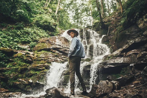 旅行和流浪概念 时尚时髦的男子在帽子与照片相机 站在瀑布在森林中的山 探索森林的旅行者 文本空间 — 图库照片