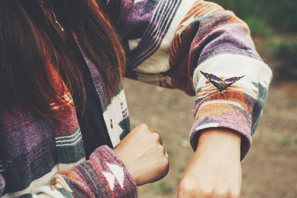 beautiful butterfly on girl hand. stylish hipster,happy woman in hat holding apatura iris  on fingers in forest in mountains. travel and wanderlust concept. space for text. amazing moment