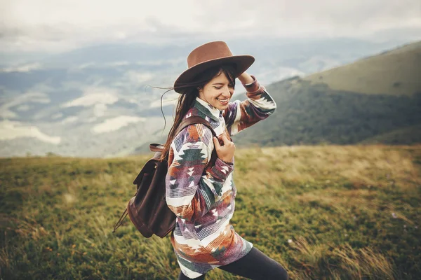 旅と放浪癖の概念 流行の旅行者内気な少女をバックパックと風が髪の毛の帽子を保持している雲で山の中を歩きます 夏休み テキストのためのスペース 素晴らしい大気瞬間 — ストック写真