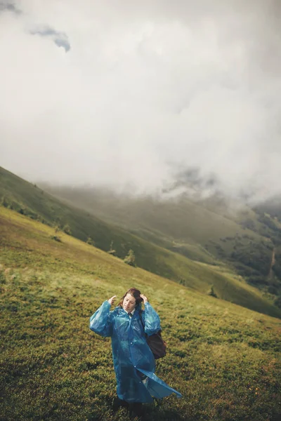 旅行者时髦的女孩在蓝色雨衣与背包 探索薄雾山 文本的空间 大气时刻 旅行和流浪概念 在山上漫步的女人 — 图库照片