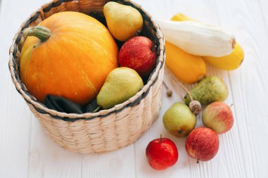 Merhaba sonbahar kavramı ve sonbaharda hasat. Kabak ve elma ve armut beyaz ahşap arka planda ışık, metin için yer ile şık hasır sepet içinde kabak. Şükran günün kutlu olsun