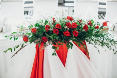 şık düğün tablo ayarı merkezinde. şık düğün masa kırmızı gül dekorasyon ve beyaz ipek sandalyeler ve peçeteler. lüks restoranda düğün için catering