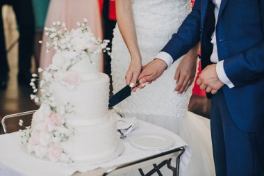 Gelin ve elinde bıçak ve şık kesme damat düğün pastası çiçekli Beyaz. pembe ve beyaz güller ile modern büyük düğün pastası. lüks restoranda yemek. Düğün