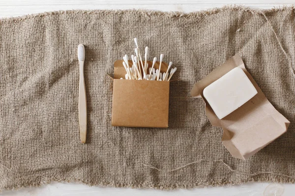 natural eco handmade coconut soap, bamboo toothbrush, ear sticks on rustic fabric, flat lay. plastic free items for personal hygiene. sustainable lifestyle, zero waste concept.