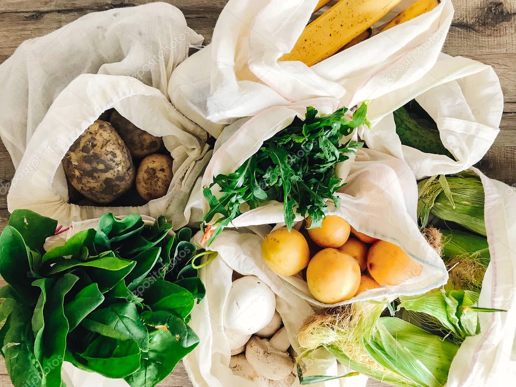 zero waste shopping concept. fresh vegetables in eco cotton bags on table in the kitchen. lettuce, corn, potatoes, apricots, bananas, rucola, mushrooms from market.  ban plastic