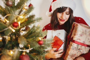 mutlu kız santa şapka şenlikli odasında birçok hediye kutuları altın güzel Noel ağacı ışıkları, holding. mutlu kış tatil atmosferik anlar. mevsim selam. Mutlu Noeller