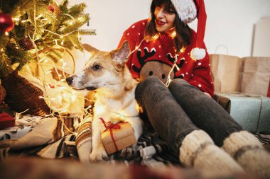 mutlu kız santa şapka şenlikli oda ışıkları ile altın güzel Noel ağacı arka plan üzerinde sevimli köpek ile sarılma içinde. Aile sıcak atmosferik anlar. kış tatili