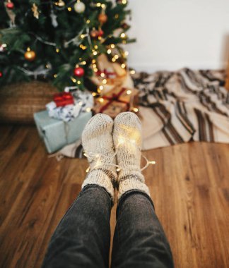 şık sıcak çorap ile oturan kız bacaklar hediyeler ve hediyeler ile Noel ağacı ışıkları garland. Festival odasında halı çorap. dekor için kış tatil. atmosferik an