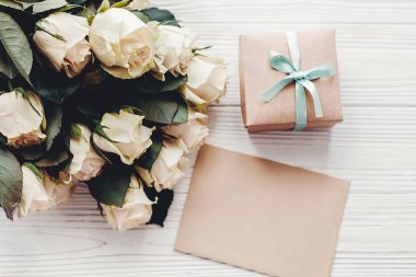 Metin için yer boş oyun kağıdı ve hediye kutusu, düz ahşap arka plan üzerinde beyaz gül yatırın. Çiçek tebrik kartı mockup. Düğün davetiyesi, mutlu anne gün kavramı. Sevgililer günü