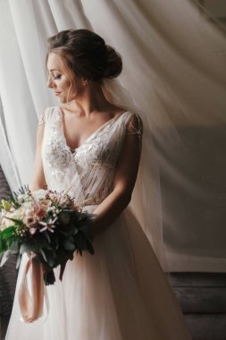 Muhteşem güzel gelin buketi yumuşak ışık penceresinde, poz ile. Şık elbise ve gülümseyen ve rüya mükemmel makyaj ile mutlu gelin. Gelin sabah. Romantik an