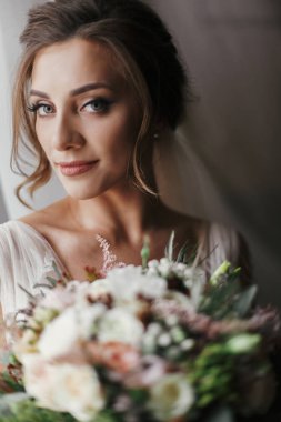 Muhteşem güzel gelin buketi yumuşak ışık penceresinde, poz ile. Şık elbise ve gülümseyen ve rüya mükemmel makyaj ile mutlu gelin. Gelin sabah. Romantik an