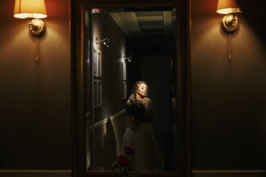 Buket ışık karanlık koridorda poz ile muhteşem güzel gelin. Ayna ayakta ve rüya mutlu şık gelin. Samimiyet kavramı. Gelin sabah