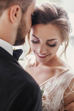 Muhteşem gelin ve yavaşça sarılma ve pencere ışıkta kucaklayan şık damat. Işıkta öpüşme şehvetli düğün çifti. Yeni evliler romantik anlar. Düğün fotoğraf