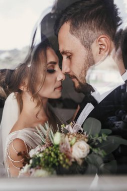 Muhteşem gelin ve şık damat yavaşça pencereye sarılma. Şehvetli düğün çifti kucaklayan. Yeni evliler romantik anlar. Yaratıcı düğün fotoğraf camı. Kopya alanı