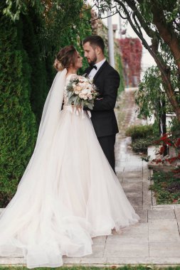 Muhteşem gelin ve şık damat hafifçe yeşil ağaçlar arka plan üzerinde sarılma. Şehvetli düğün çifti kucaklayan. Yeni evliler romantik anlar. Modern düğün fotoğraf