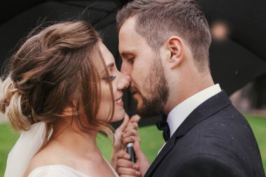 Muhteşem gelin ve şık damat tutkuyla yağmurlu havada şemsiyesi altında öpüşme. Şehvetli düğün çifti kucaklayan. Yeni evliler romantik anlar. Modern düğün fotoğraf