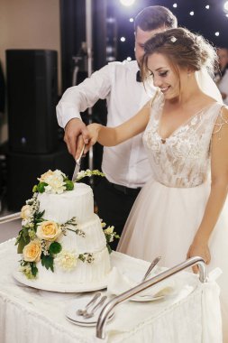 Muhteşem gelin ve birlikte kesme şık damat düğün pastası düğün Resepsiyon güllü beyaz. Mutlu evlilik çift Pasta tatmak. Yeni evliler romantik anları