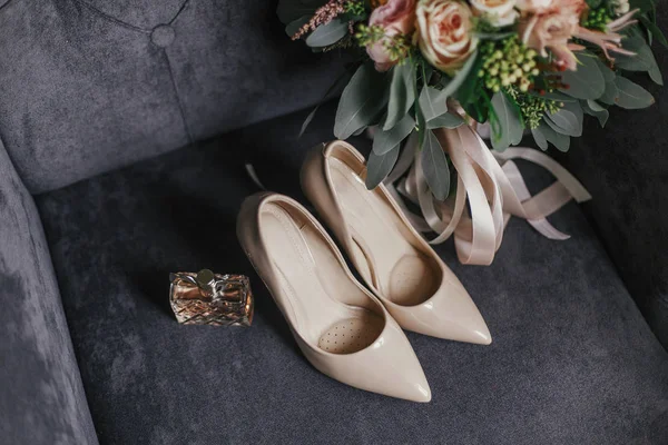 现代婚礼花束粉红色玫瑰和绿桉树与粉红色丝带 米色鞋和香水瓶在时尚灰色沙发上 婚礼安排的当代构成 — 图库照片