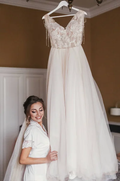 Linda Noiva Roupão Seda Olhando Para Vestido Noiva Elegante Pendurado — Fotografia de Stock