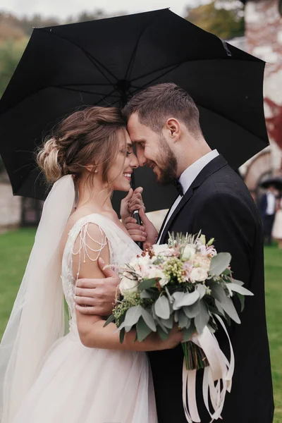 Prachtige Bruid Stijlvolle Bruidegom Voorzichtig Knuffelen Onder Paraplu Regenachtige Buitenshuis — Stockfoto