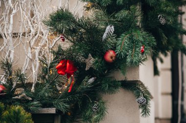 Şık Noel süsleri, yeşil Noel çelenk kırmızı yay ve süs eşyaları, çam kozalakları, yıldız ile beyaz Avrupa şehri sokakta dalları. Festival dekor şehir merkezi, kış tatili