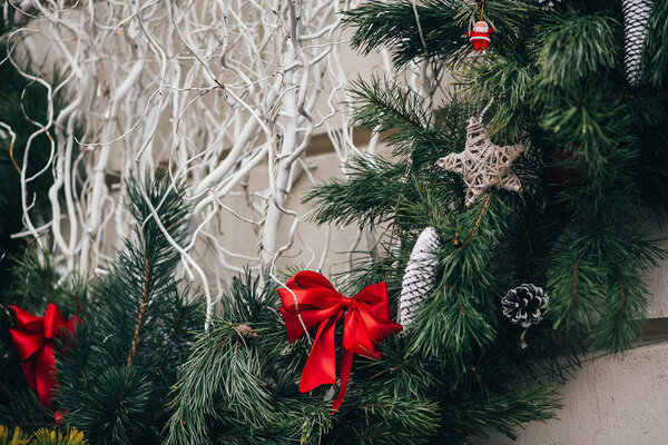 Stylish christmas decorations, green christmas wreath with red bows and ornaments, pine cones, stars, white branches in european city street. Festive decor in city center, winter holidays