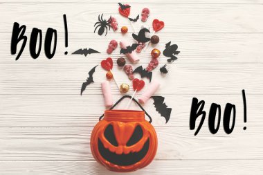 Boo! metin işareti. Cadılar Bayramınız Kutlu Olsun. O fener kova tatil şeker, yarasalar, örümcekler, beyaz rustik ahşap zemin üzerinde kafatasları ile jack. Sezonun tebrik kartı. Hediye ver yoksa karışmam