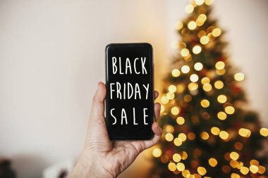 Siyah Cuma büyük bir satış metin. Tatil indirim teklif. El altın güzel Noel ağacı ışıkları Festival odasında ile arka plan üzerinde telefon tutarak.