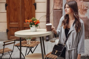 Şehirdeki sokak ahşap masa gülümseyen fincan kahve ve çanta, tutan güzel genç kadın. Şık mutlu hippi kız gülümseyerek, kafe Teras vaktinizi güzel saçlı