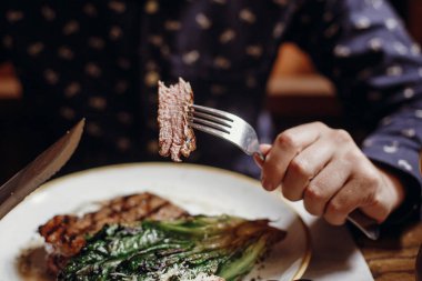 Çatal ve bıçak tutarak ve lezzetli sulu biftek ızgara lahana, domates ve peynir ile şehir sokak kafede masada yemek eller. Barbekü Restoran sebzeli tatma adam